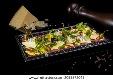 Elegant Beef Carpaccio, Italian Appetizer, Presentation on Black Plate and Background 