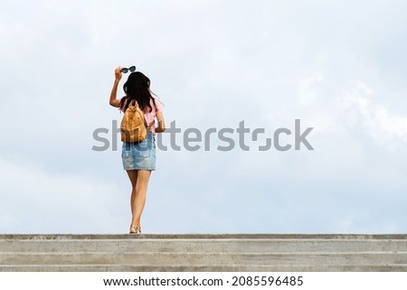 The figure of a girl with a yellow backpack on the background of a cloudy sky. View from the back. Unrecognizable person. Copy space