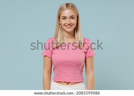 Young smiling happy cheerful beautiful caucasian blonde woman 20s wearing casual pink t-shirt looking camera isolated on plain pastel light blue background studio portrait. People lifestyle concept