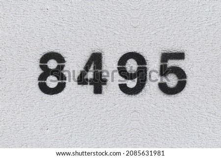 Black Number 8495 on the white wall. Spray paint. Number eight thousand four hundred ninety five.