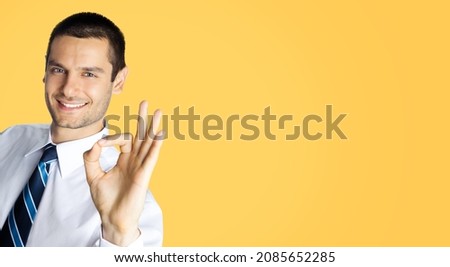 Portrait of smiling businessman in white shirt and tie, showing okay ok zero 0 hand sign gesture, over orange yellow colour background. Happy confident man gesturing. Business success concept. Male.