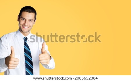 Businessman in confident white shirt and tie, showing thumb up like hand sign gesture over orange yellow color background. Happy smiling man gesturing. Success in business. Male bank manager executive