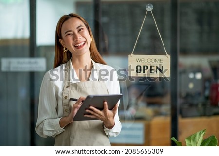 Asian Happy business woman is a waitress in an apron, the owner of the cafe stands at the door with a sign Open waiting for customers. Small business concept, cafes, and restaurants 