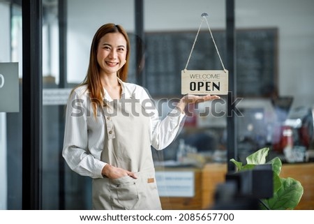 Asian Happy businesswoman is a waitress in an apron, the owner of the cafe stands at the door with a sign Open waiting for customers. Small business concept, cafes, and restaurants 
