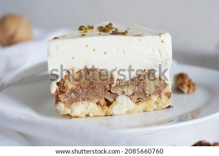 A piece of cake in a plate lies on a white table. There is a towel and walnuts next to the cake.