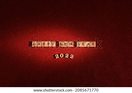 Happy New Year 2022. text on wooden blocks on an iridescent red background with sequins