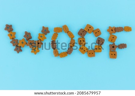 Inscription Woof isolated on blue background. Text from mix dry pet food. Top view