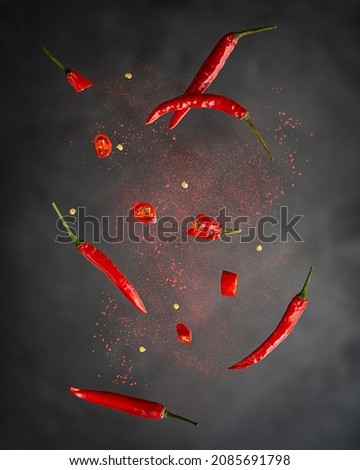 Levitation or flying of red chili pepper whole and slices with paprika powder used for food seasoning to make hot spicy flavour in mexican and asian cuisine against dark black background. Vertical Royalty-Free Stock Photo #2085691798