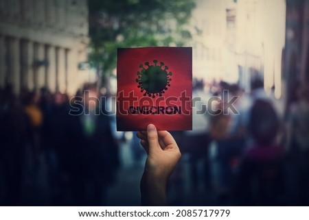 Omicron the new variant of the Covid-19 virus, coronavirus mutations, sars-cov-2 strain. Hand holds red banner warning in the crowded streets. Another wave of pandemic outbreak Royalty-Free Stock Photo #2085717979