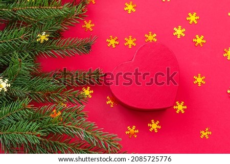 Christmas flatlay on a red background: spruce branches, golden confetti and a red heart-shaped gift box. Concept greetings for Christmas, New Year, advertising poster of Christmas jewelry sale
