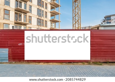Blank white advertising banner on the fence of construction site. Residential area with modern buildings on a sunny day.