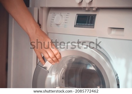 A male hand opens the door of a new washing machine in his modern, bright bathroom, close-up. The man washes clothes in the laundry. Royalty-Free Stock Photo #2085772462