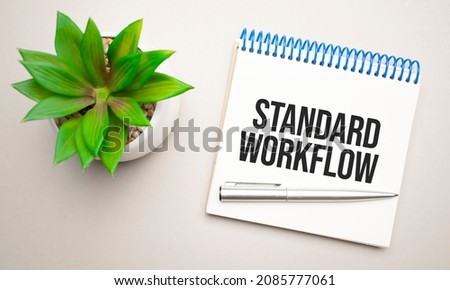 Standard workflow is written in a white notepad near a clipboard, calculator, green plant, glasses and a pen on a yellow and concrete background. Business concept. Flat lay.