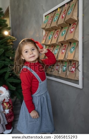 handmade advent calendar hanging on the wall, child girl standing near craft bags with sweets, festive entertainment for children, winter traditions, Christmas advent calendar concept