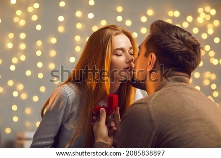 Happy young couple in love kissing after the girl has said yes and accepted marriage proposal and diamond engagement ring. Man enjoying romantic date with his girlfriend and giving her new jewelry