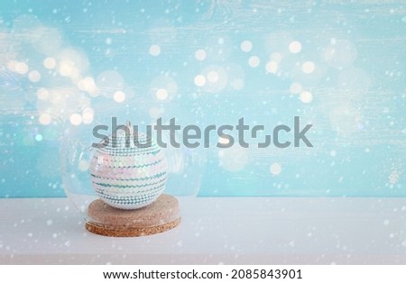 image of christmas tree decoration inside glass ball over white wooden table and pastel blue background