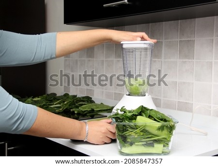 Preparation of green juice, the vegetables are chopped on the wooden board and put in the blender in the kitchen for healthy and dietary breakfast
