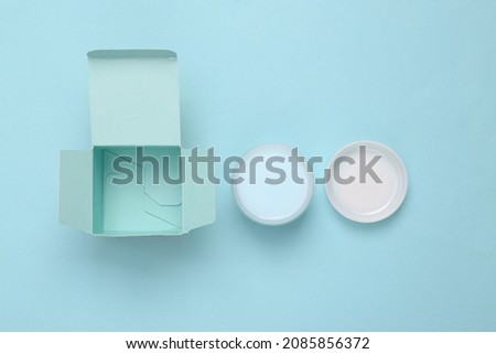Cardboard box with jar of cream on blue background
