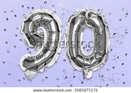 Silver foil balloon number, digit ninety on a lilac background with sequins. Birthday greeting card with inscription 90. Anniversary concept. Top view. Numerical digit. Celebration event, template.