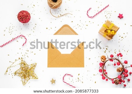 Open brown envelope with blank white card and Christmas decorations, candy canes and gift box on white background. Top view, flat lay, mock up.