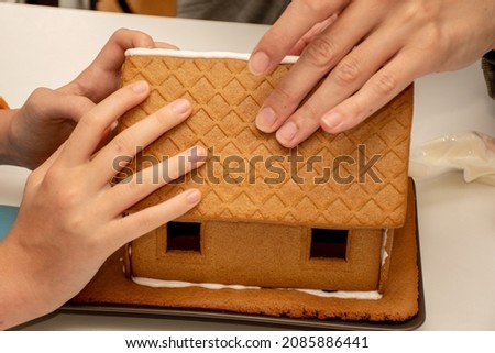 Building assembling of a gingerbread house with royal icing in four hands. Christmas family moments concept