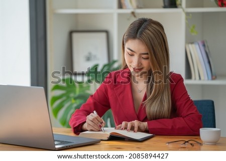 Businesswoman writing a note while using laptop at a table in an office.	