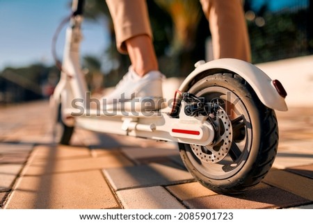 Close-up image of female feet on an electric scooter, with a wheel in the foreground. Royalty-Free Stock Photo #2085901723
