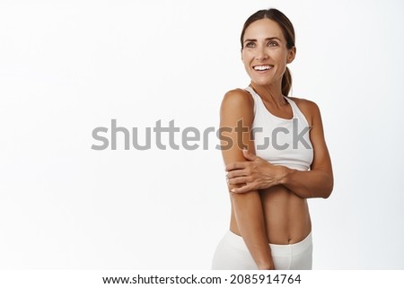 Middle aged 30 years old fitness woman with fit and strong body, abs and muscles, looking aside happy and smiling, exercise in gym, workout indoors, white background Royalty-Free Stock Photo #2085914764