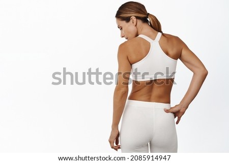 Rear view of middle aged sports woman back, masculine and fit body, standing in activewear against white background Royalty-Free Stock Photo #2085914947