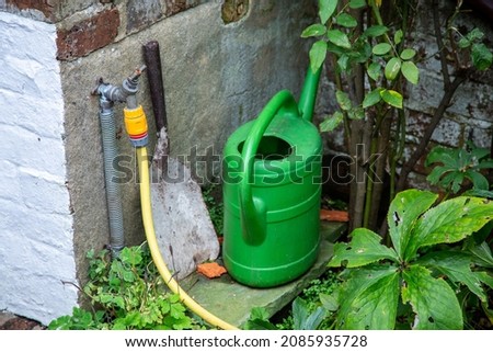 Green watering can, yellow hose and metal shovel in an urban back garden