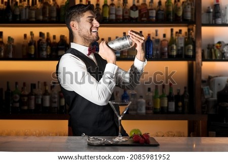 Cool professional bartender making a cocktail, shaking a cocktail shaker. Authentic barman making alcohol beverages in modern bar. High quality photo. Royalty-Free Stock Photo #2085981952