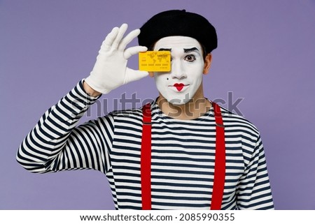 Charismatic bright young mime man with white face mask wears striped shirt beret holding in hand close cover eye with credit bank card isolated on plain pastel light violet background studio portrait