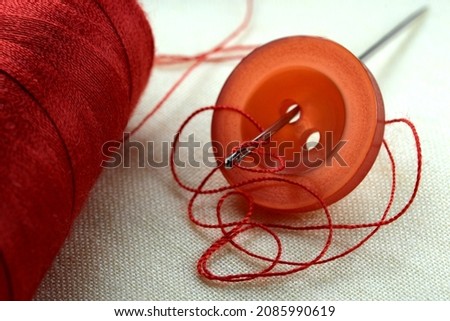 Red button with a needle with inserted thread on a white linen cloth close-up macro photography