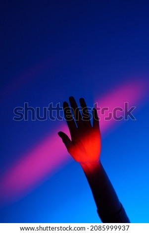 Closeup of anonymous woman arm gesturing with open hand over fashion blue wall, neon red stripe on wrist and background. Colorful light, minimalism concept.  Royalty-Free Stock Photo #2085999937