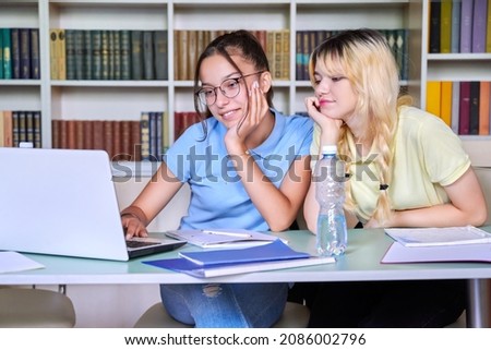 Two teenage schoolgirls students sitting with a laptop in the library
