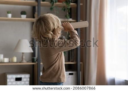 Little preschool adorable boy holding toy cardboard spyglass, looking forward at window at home. Sweet kid playing game with paper homemade craft tube telescope, having fun, imagining adventures Royalty-Free Stock Photo #2086007866