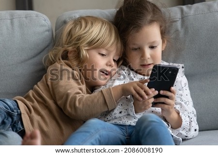 Two little toddler preschooler sibling gen Z kids using online parental control app on mobile phone, playing video game for children, sharing digital gadget, relaxing on comfortable couch at home Royalty-Free Stock Photo #2086008190
