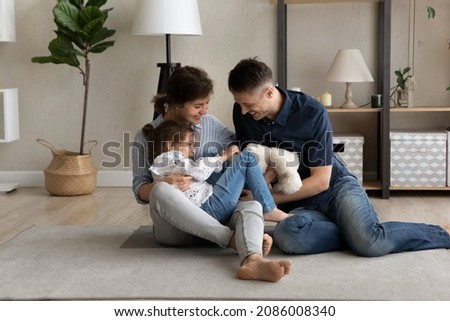 Happy laughing parents cuddling and tickling sweet little daughter girl on heating floor at home, having fun together. Excited mom, dad, kid playing, feeling joy, giggling. Family playtime Royalty-Free Stock Photo #2086008340