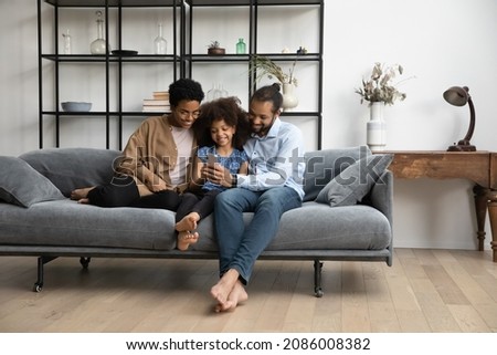 Full length addicted to modern technology bonding loving young African American couple parents using smartphone with happy cute little kid daughter, enjoying playing games or making funny photos.