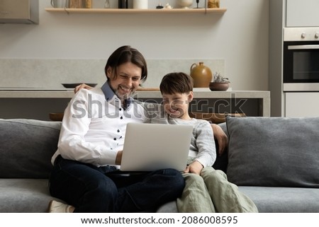 Happy two male generations family using computer sitting on couch at home. Joyful 40s young father and teenage schoolboy son watching funny movies online, shopping in internet store or web surfing.