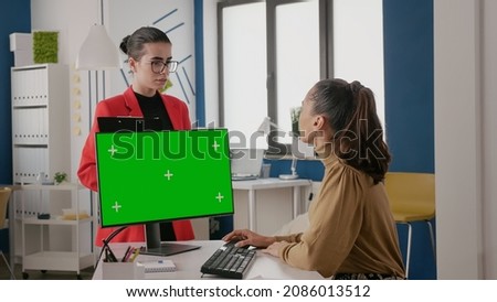 Women doing teamwork with green screen on computer, colleagues using isolated mock up template with chroma key copy space on monitor display. Blank copy space background in office.