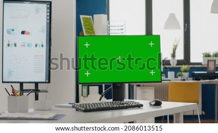 Close up of monitor with green screen at empty desk. Nobody in startup office with chroma key and isolated mock up template on computer display. Mock-up copy space with blank screen.