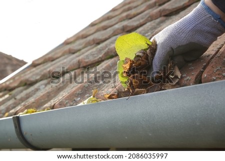 Cleaning the gutter from autumn leaves before winter season. Roof gutter cleaning process.	 Royalty-Free Stock Photo #2086035997