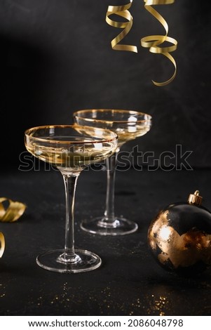 New Year champagne glasses and Christmas gold decorations on black background. Vertical composition. Close up.