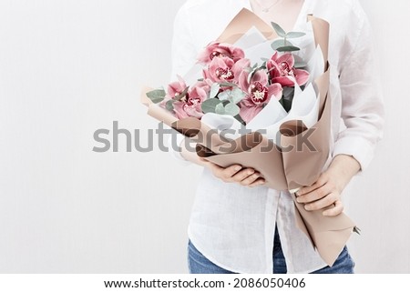 Blossoming delicate flowers of pink orchid in hands of female on light background with copy space. Modern bouquet to gift for your mother or friend.