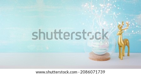 Image of christmas ball and gold deer in front of pastel blue background