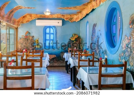 Interior of a fish restaurant decorated in a blue colour. Spacious restaurant hall is empty, there are no visitors at the tables. Large windows offer city views Royalty-Free Stock Photo #2086071982