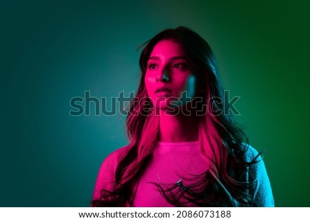 Calm. Studio shot of young adorable cute girl, student in casual style clothes posing isolated on dark green studio backgroud in pink neon light. Emotions, facial expression, youth, fashion and ad