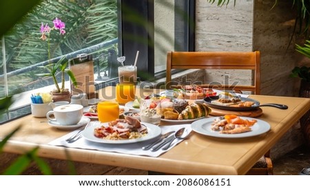 Breakfast in luxury hotel. Table full of various food from buffet in modern resort. Morning food - fresh bakery, glasses of orange juice, eggs, cold cuts and plate with tropical fruits in restaurant Royalty-Free Stock Photo #2086086151