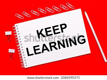 On a bright red background, a white pencil, white paper clips, and a white notebook with the text KEEP LEARNING